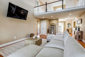 Een ruime woonkamer met een grote hoekbank, een flatscreen televisie aan de muur en een balkon met een hekwerk.