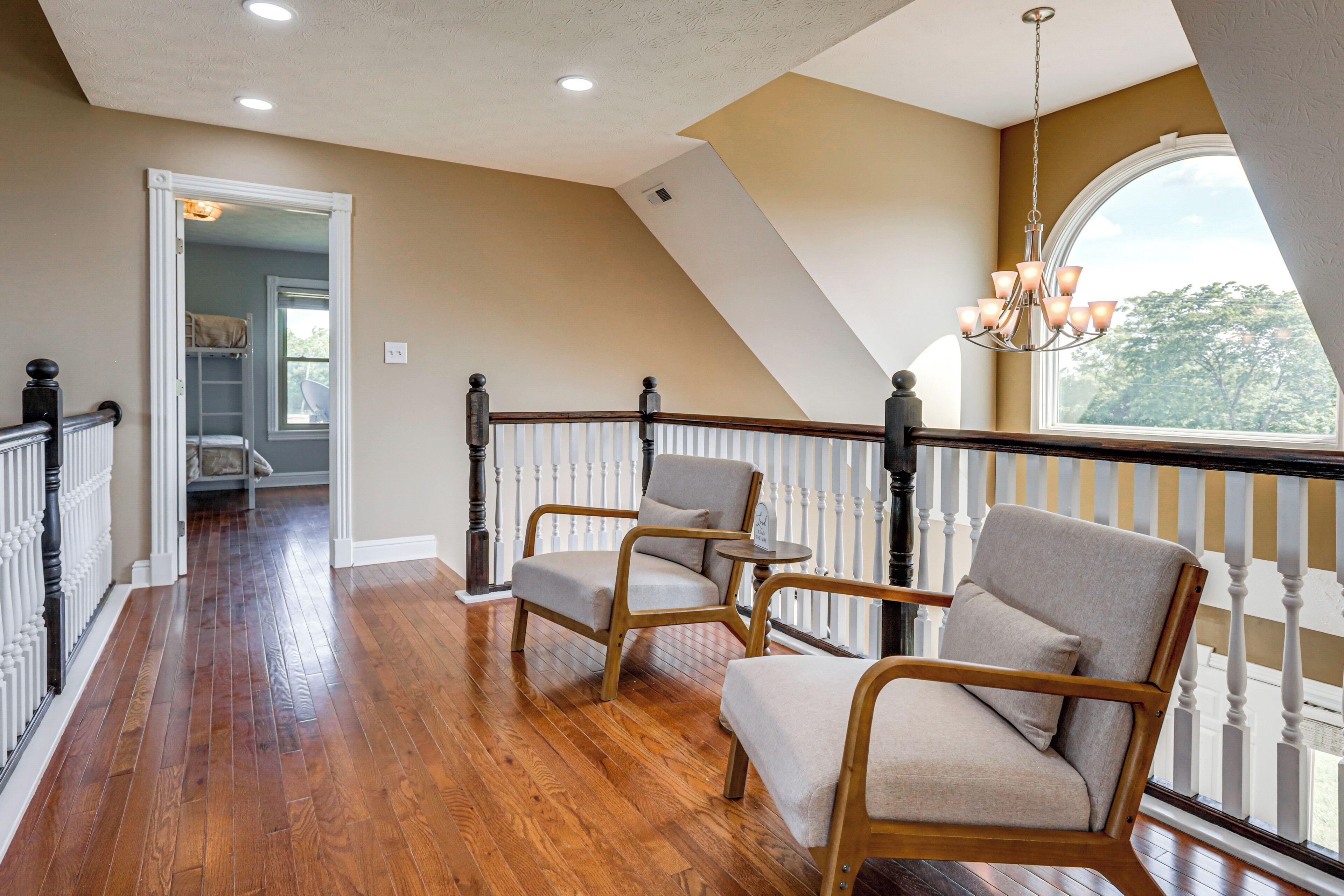 A spacious balcony with wooden flooring, two upholstered chairs, a small round table, and a chandelier.