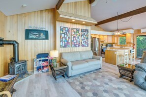 Una sala de estar acogedora con sofá, pared de madera, un cuadro, una zona de cocina con barra y un ventanal grande.