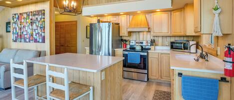 Una cocina compacta con una isla central, armarios de madera, un refrigerador, estufa y microondas.