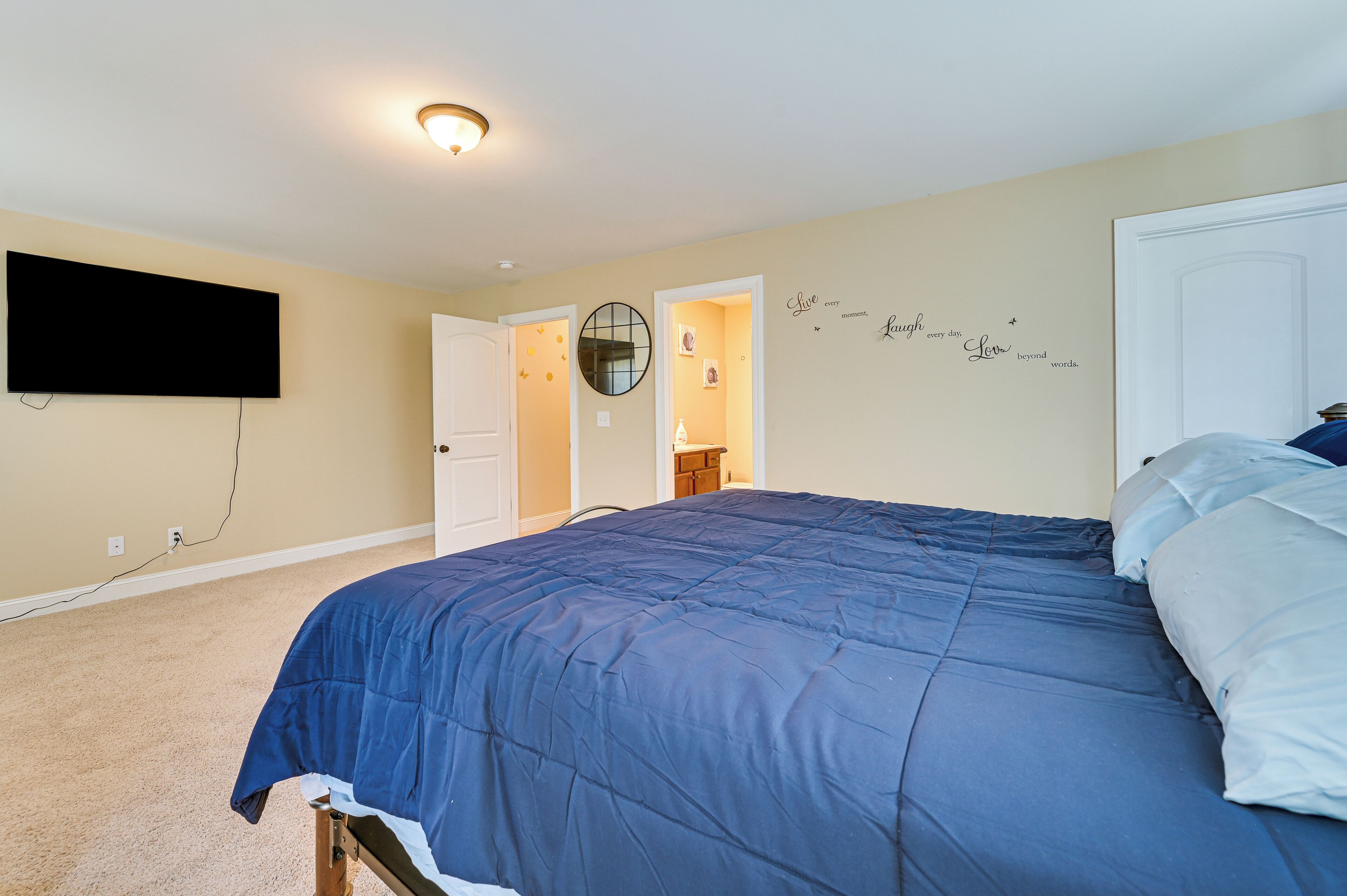 Un dormitorio con una cama grande, un televisor montado en la pared y una puerta que da a otra habitación.