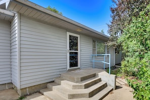 A house with a front door, a set of concrete steps leading to the door, and a small garden area with plants and a blue railing.