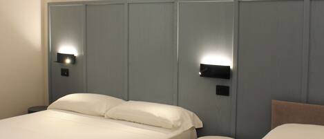 A hotel room with two beds, a bedside table, and a nightstand with a lamp.