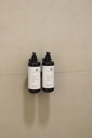 Dos botellas negras con etiquetas blancas sobre un muro de azulejos.