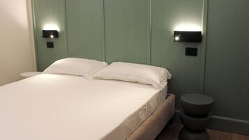 Een bed met witte lakens, een hoofdbord met wandlampen en een rond nachtkastje.