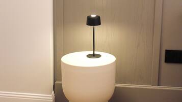 Una moderna mesita de noche minimalista con una lámpara, ubicada sobre un piso de madera y cerca de una puerta.