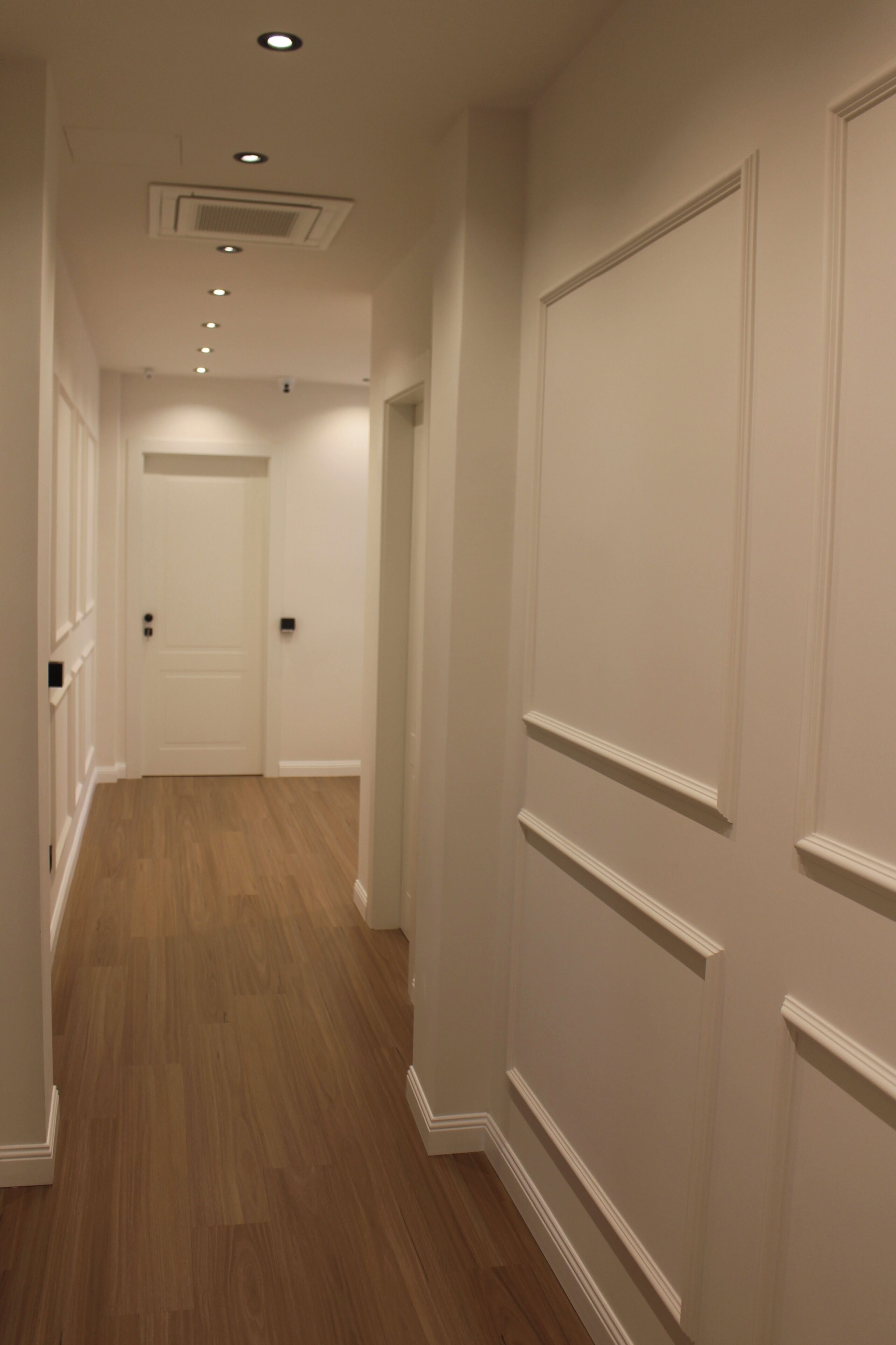 A hallway with wooden flooring, white walls, and a door at the end.