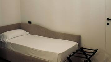 Una stanza piccola con un letto singolo, pavimento in legno, un comodino e una mensola a parete.