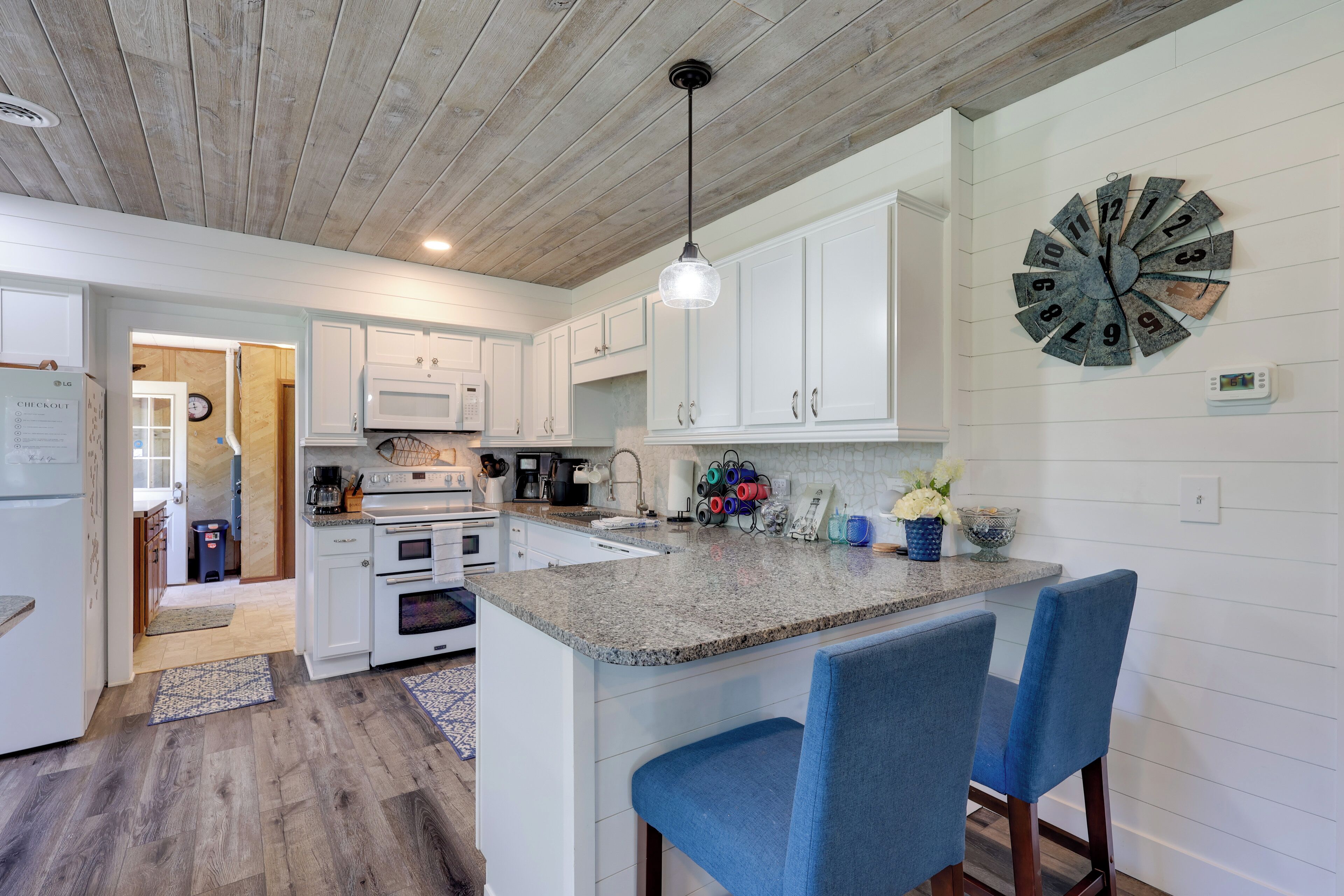 A modern kitchen with white cabinetry, a granite countertop, and a unique clock.