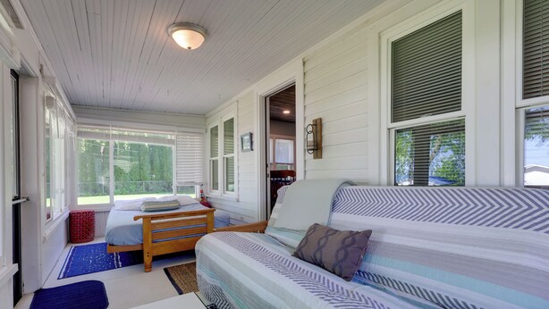 A bedroom with a bed, a wooden bench, a small table, and a window with blinds. - Cute Cottage Getaway; Walk to Lake and Town (Port Sanilac)