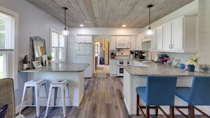 A modern kitchen with white cabinets, a wooden ceiling, and bar stools. - Cute Cottage Getaway; Walk to Lake and Town (Port Sanilac)