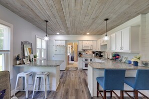 A modern kitchen with white cabinets, a wooden ceiling, and bar stools.