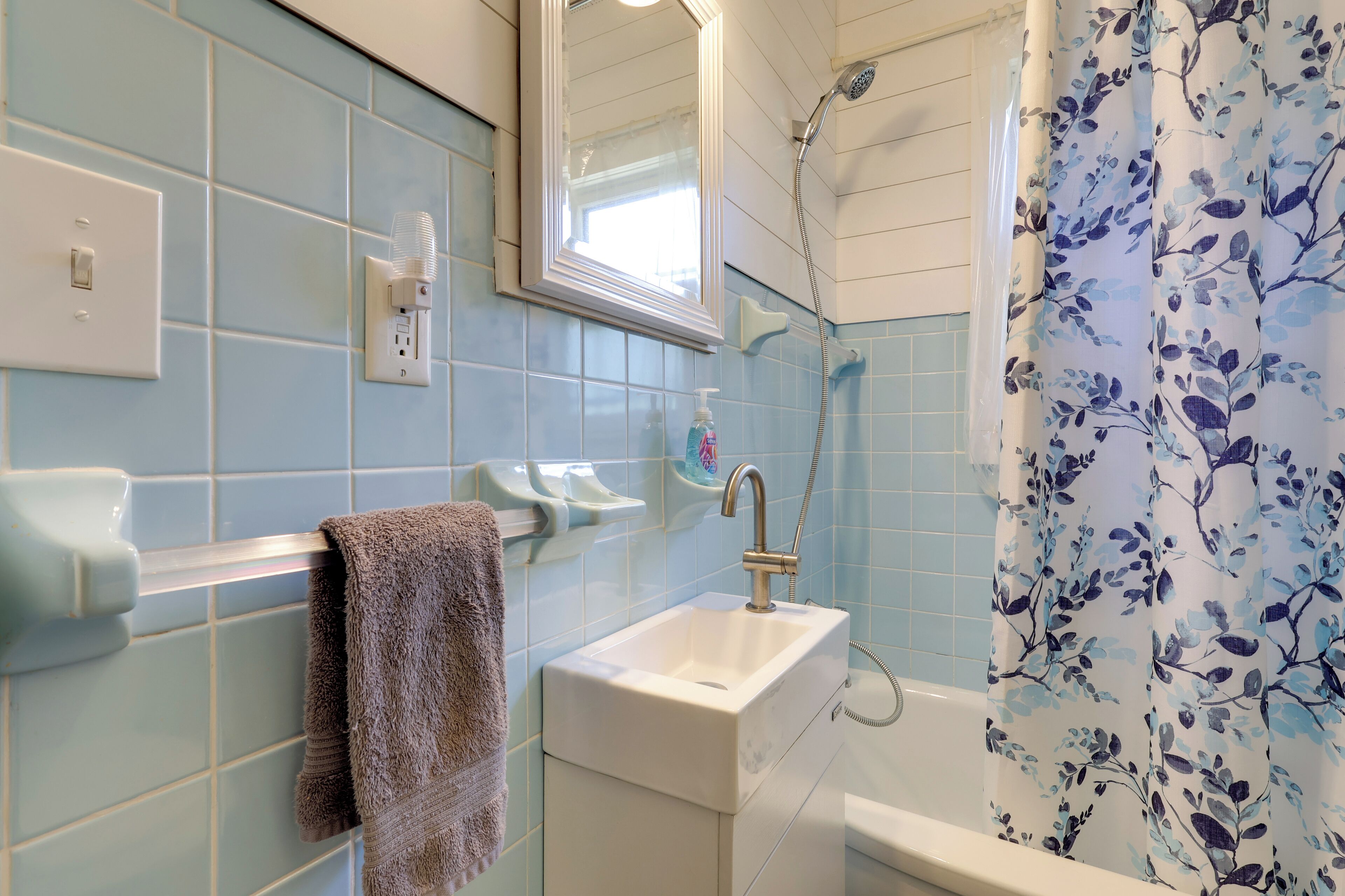 A bathroom with a sink, mirror, shower, and floral shower curtain.