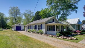 A two-story house with a covered porch, a garage, and a well-maintained lawn. - Cute Cottage Getaway; Walk to Lake and Town (Port Sanilac)