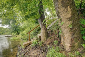 A wooden staircase leading up to a stone platform by a river, surrounded by lush greenery.