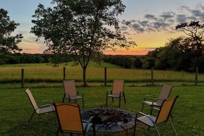 A grassy outdoor area with four chairs arranged around a fire pit.