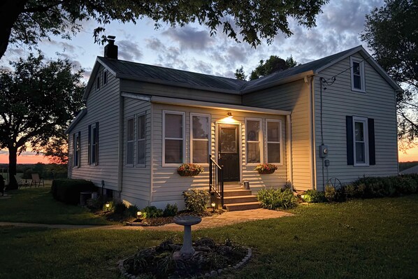 A two-story house with a front porch, a small garden with a birdbath, and a chimney.