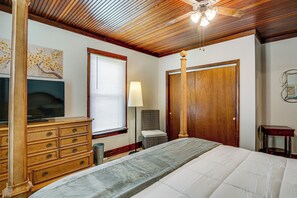 A bedroom with a wooden ceiling, a bed, a dresser, a television, a window with blinds, and a door.