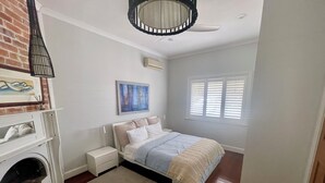 Een slaapkamer met een bed, nachtkastje, wanddecoratie, open haard en een raam met jaloezieën.