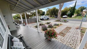 Een overdekte veranda met een bankje, een bloemenplanter en een bekleed bloembed.