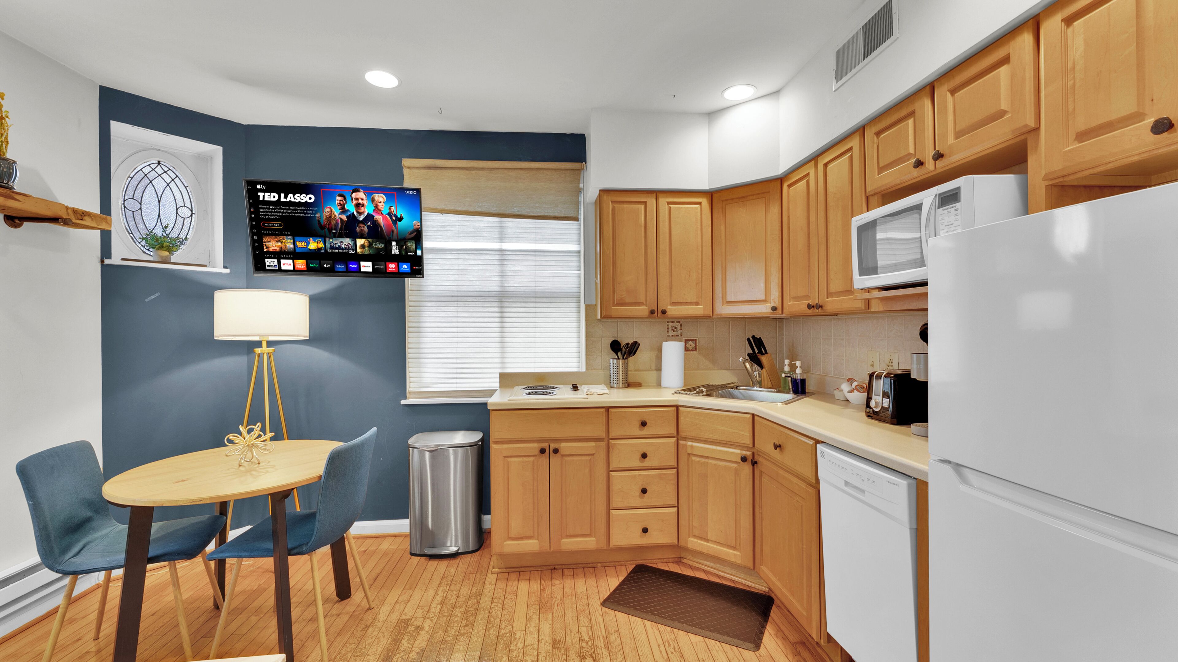 A compact kitchen with wooden cabinets, a microwave, a dishwasher, a sink, and a dining area with a table and chairs.