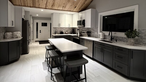 A modern kitchen with a wooden ceiling, white cabinets, a large island, and a built-in TV. - Finger Lakes, Wine Country, Modern Escape (Montour Falls)