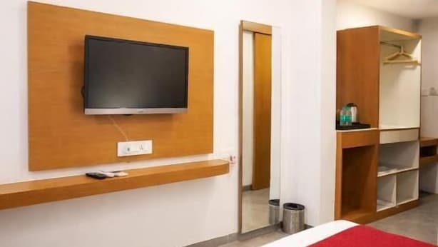A hotel room with a bed, a TV mounted on the wall, a wardrobe, and a mirror. - Hotel Paradise  (Rajgurunagar)