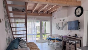 Ett rum med en säng på ett loft, ett skrivbord med en dator, en tv och en skjutdörr i glas som leder ut till utsidan.