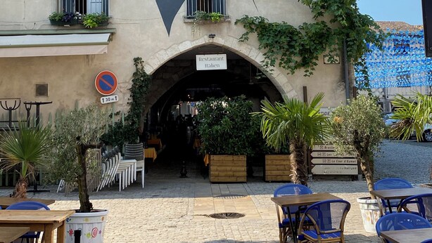 Un edificio con un mural de una pareja besándose, mesas al aire libre y un letrero que dice 'Restaurant Italien'.
