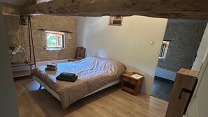 Un dormitorio con cama, vigas de madera, una ventana, un ventilador y una mesita.