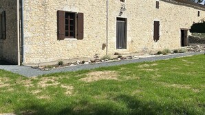 Un edificio de piedra con techo de tejas, una puerta y ventanas con contraventanas.