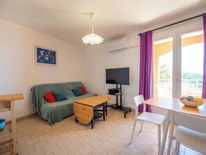 Ein möbliertes Zimmer mit einer Couch, einem Holztisch, einem Fernseher und einem Balkon mit Blick.