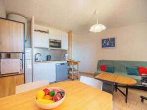 Ein kompakter Wohnbereich mit Küchenzeile, einem Essbereich mit Obstschale, einer Couch mit Kissen und einer Pendelleuchte.