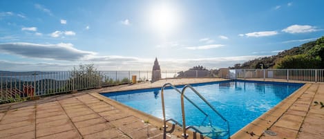 A swimming pool with a metal ladder, surrounded by a tiled deck and a metal fence.