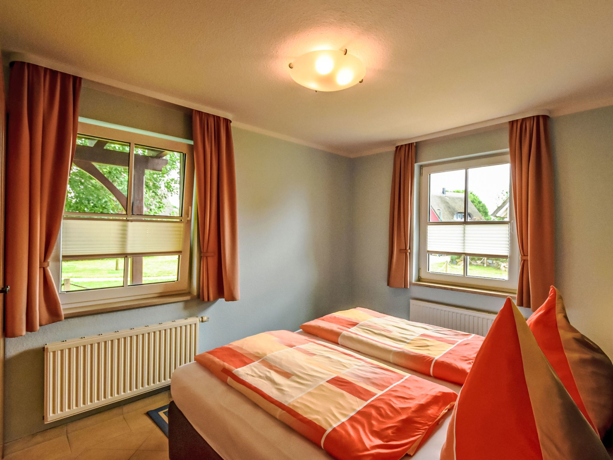 Een slaapkamer met twee ramen, een radiator en een bed met oranje en witte beddengoed.