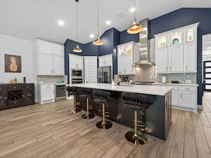 A modern kitchen with white cabinets, a large island with bar stools, stainless steel appliances, and pendant lighting. - The Pineapple Oasis Pool And Spa Retreat (Humble)