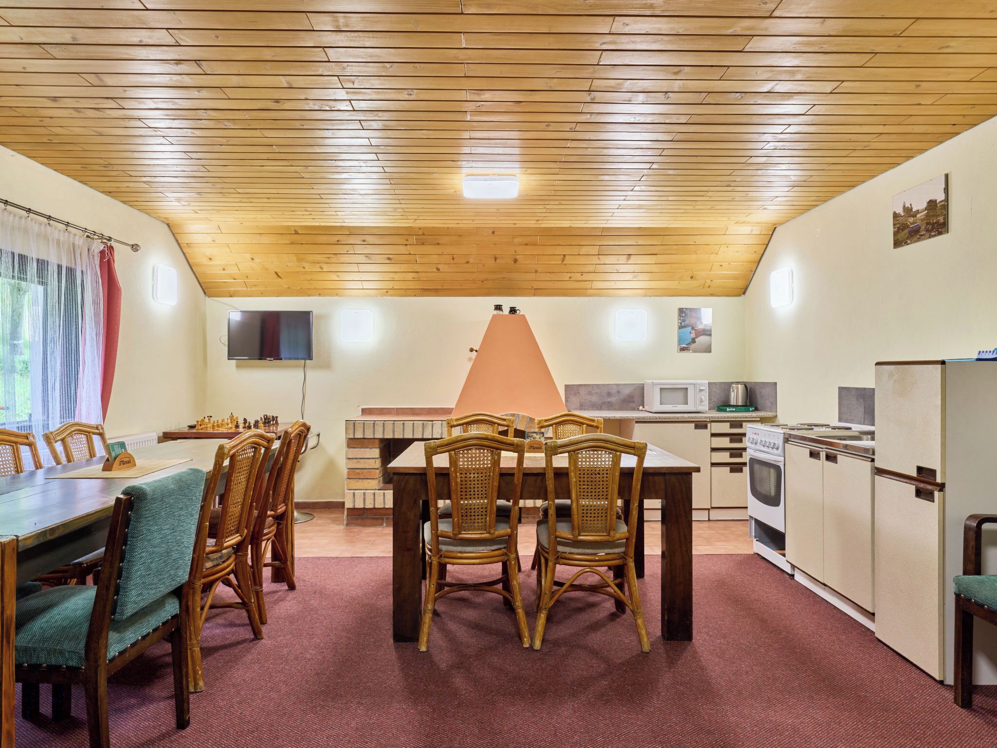 Ein Essbereich mit Holzbalkendecke, einem Backofen aus Ziegeln und einer Küche mit Mikrowelle und Kühlschrank.