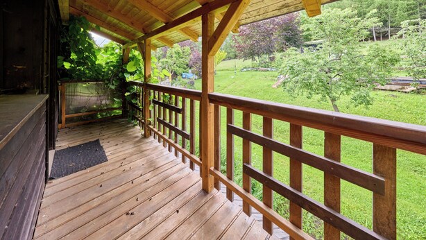 Un terrazzo in legno con ringhiera, un portico coperto e vista su un paesaggio verde.