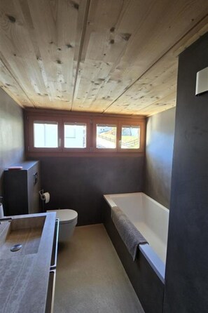 A bathroom with a bathtub, toilet, and a window. - Apartment Jörger by Interhome (Flims)