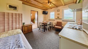 Una stanza accogliente con soffitto in legno, un letto, un tavolo da pranzo con sedie, angolo cottura e una finestra vista.