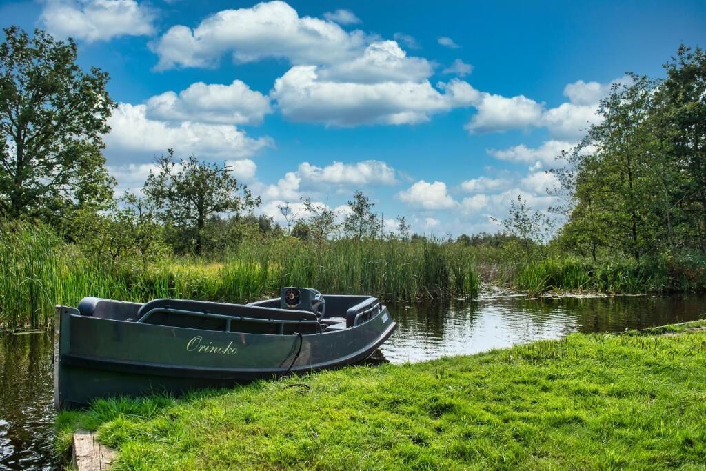 Ein Boot namens 'Orinoco' liegt an einem ruhigen Flussufer, im Hintergrund üppiges Grün und Bäume.