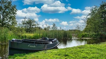 Ein Boot namens 'Orinoco' liegt an einem ruhigen Flussufer, im Hintergrund üppiges Grün und Bäume.