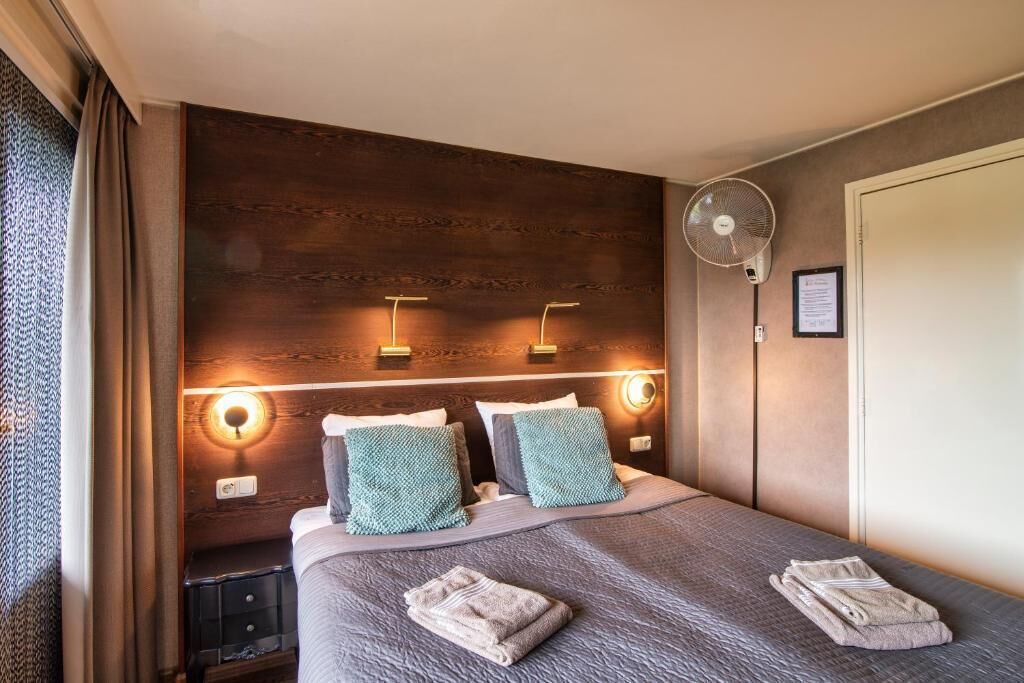 A hotel room with a bed, bedside lamps, a wall-mounted fan, and a door.