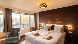 A hotel room with a large bed, a chair, a view of the outside, and a modern ceiling light fixture.