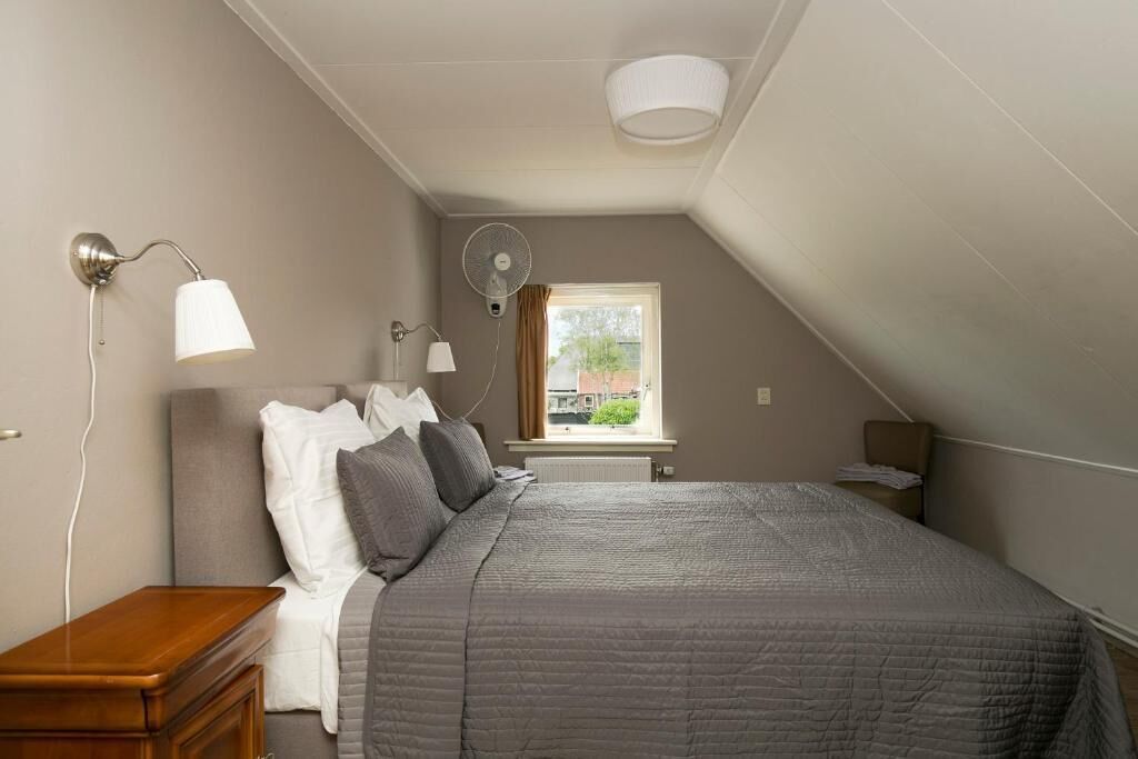 Un dormitorio con cama, lámparas de noche, mesita de noche, ventana y ventilador de techo.