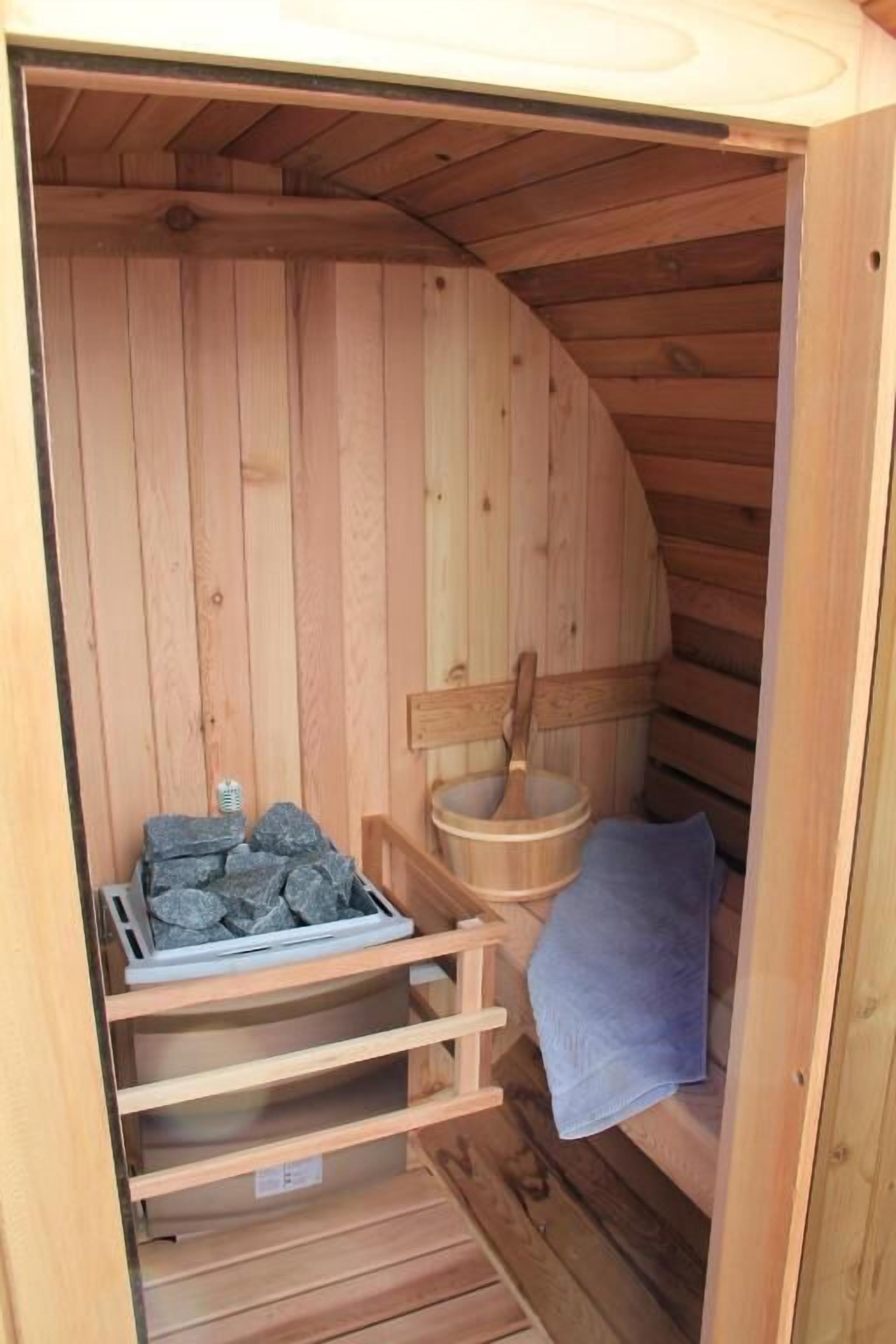 A wooden sauna with a bench, a wooden bucket, and a tray of stones.