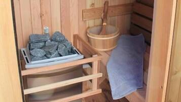 A wooden sauna with a bench, a wooden bucket, and a tray of stones.