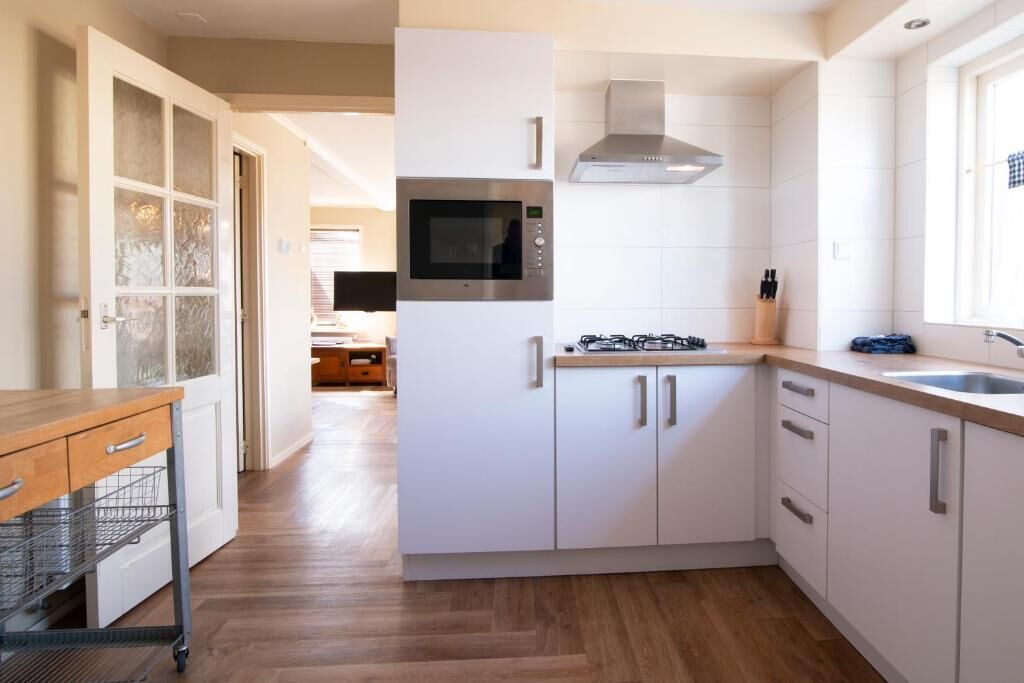 A modern kitchen with white cabinetry, a built-in microwave, a gas stove, and a stainless steel range hood.