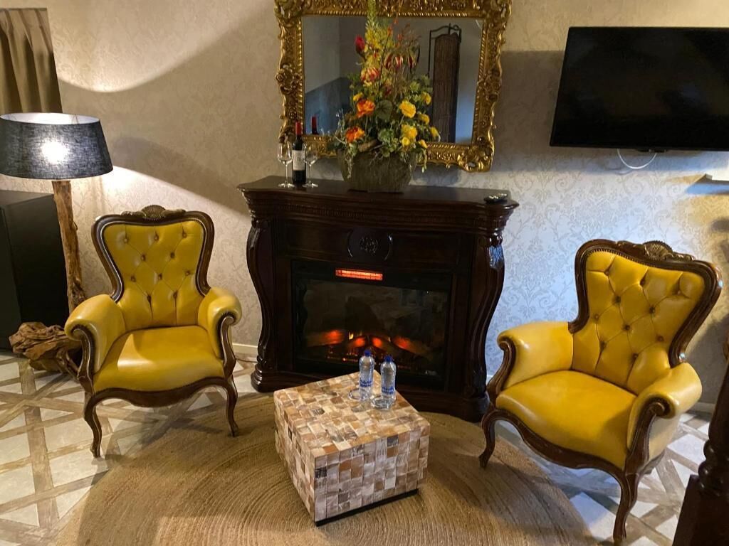A living room with two yellow armchairs, a fireplace, a television, and a mirror.