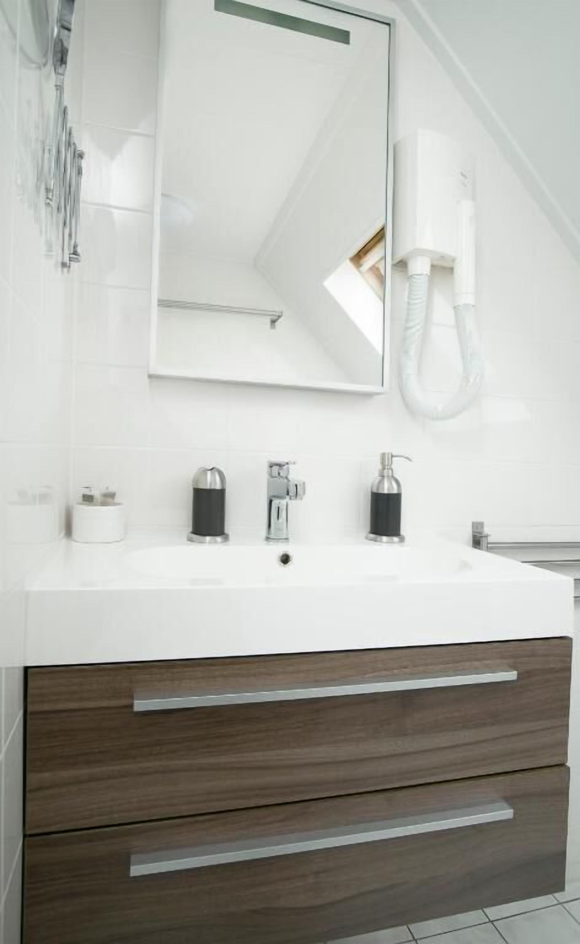 Un baño moderno con tocador blanco, un espejo grande, un teléfono de pared y un cabezal de ducha.